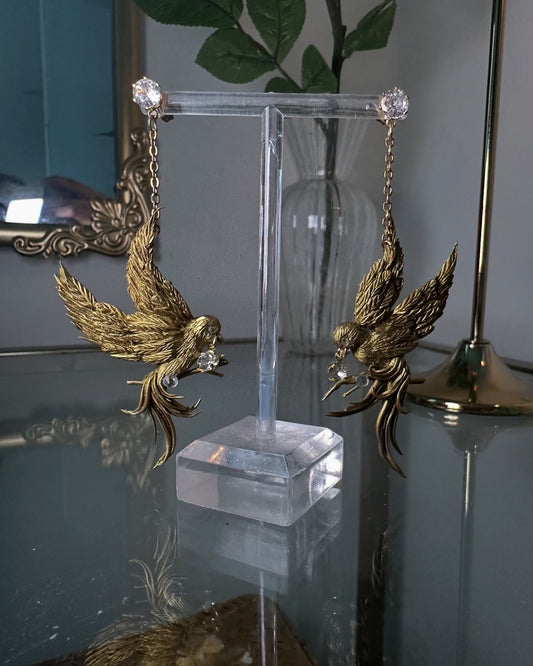 Hand-sculpted gold birds in flight, transformed into dramatic earrings with chain and crystal accents.