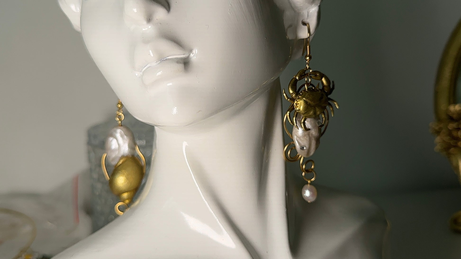 Asymmetrical ocean-inspired earrings made of polymer clay, stainless steel, and freshwater pearls, shown near the shoreline.