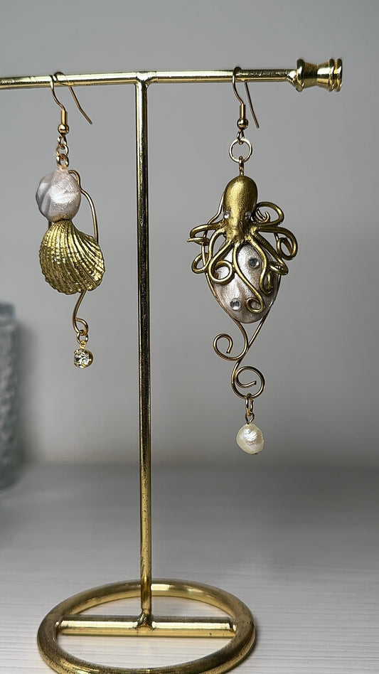 Artistic asymmetrical earrings featuring a hand-sculpted octopus and a golden seashell, with pearl and crystal details.