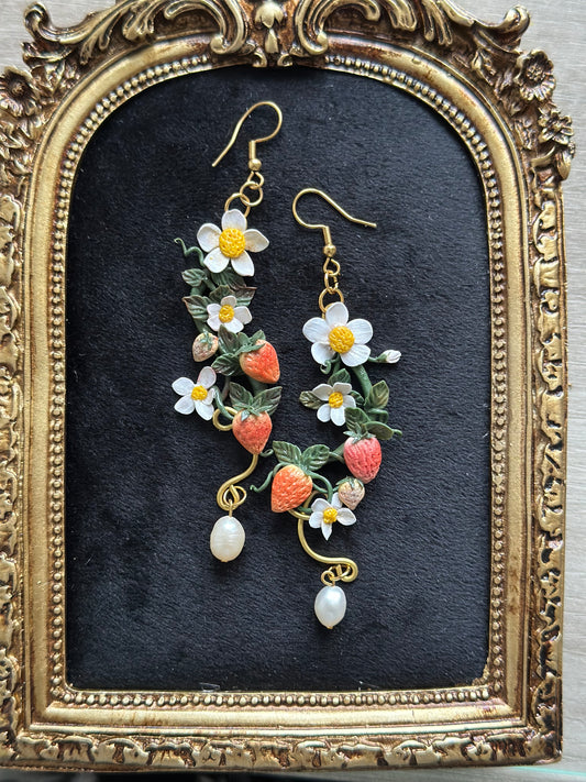 Asymmetrical handmade strawberry earrings with white strawberry flowers, green leaves, and baroque pearls, crafted in polymer clay with gold-tone hooks. Nature-inspired statement earrings perfect for summer and botanical jewelry lovers.
🇮🇹 Italiano 
Orecchini asimmetrici fatti a mano con fragole, fiori di fragola bianchi, foglie verdi e perle barocche, realizzati in pasta polimerica con ganci dorati. Gioielli ispirati alla natura, ideali per l’estate e per chi ama gli accessori botanic