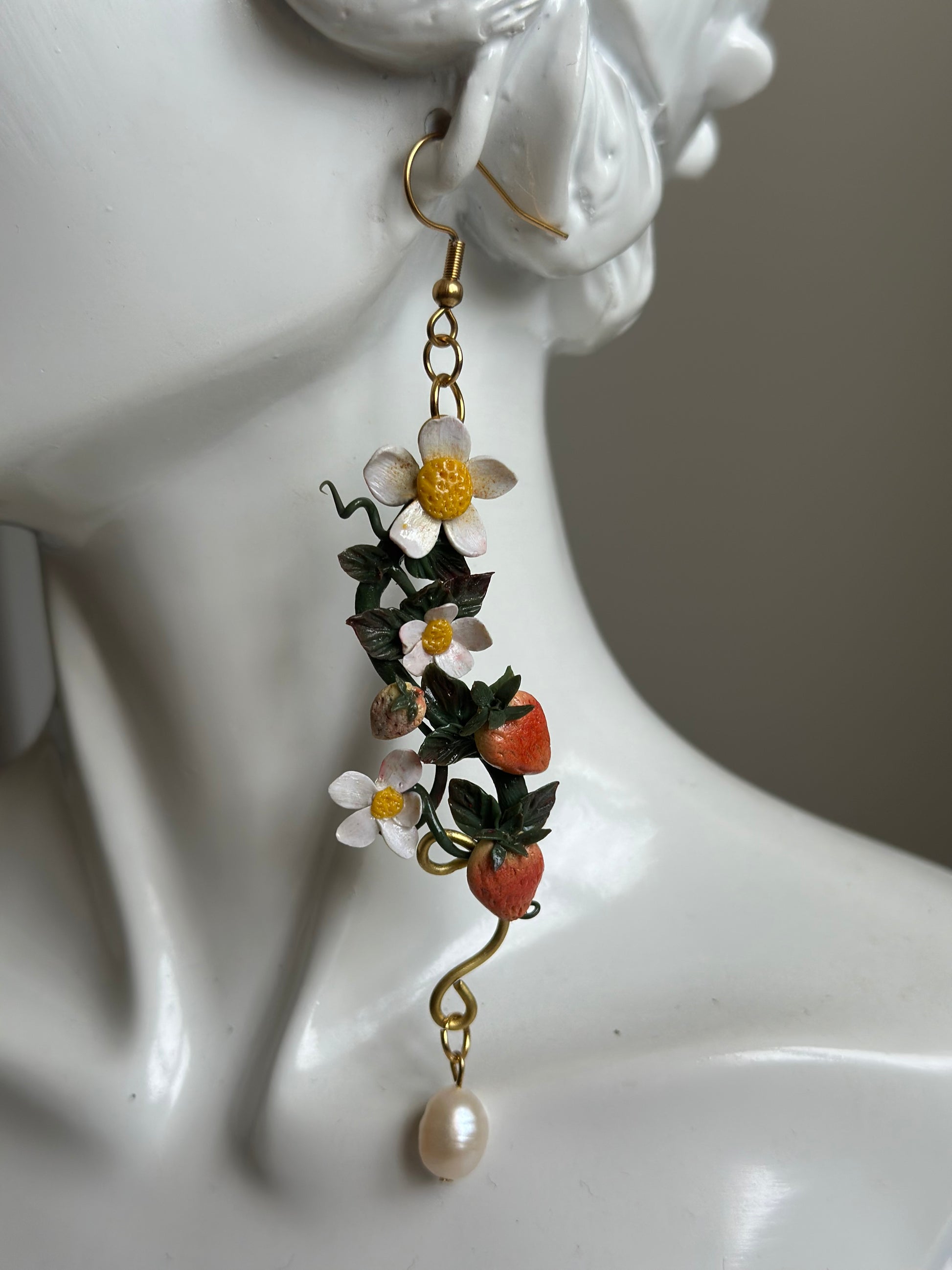 Model wearing handmade strawberry and flower polymer clay earring with pearl accent.