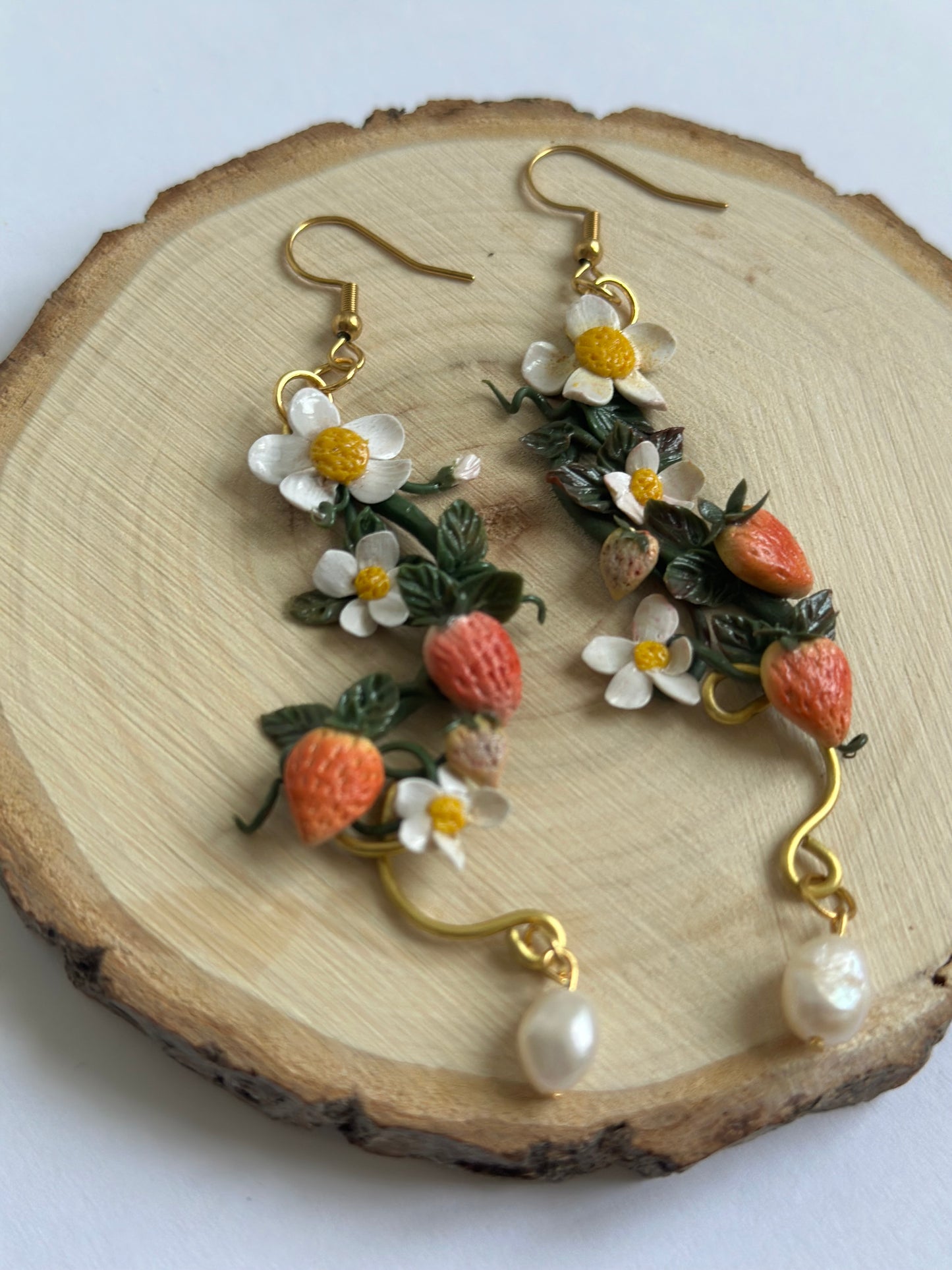 Orecchino artigianale in pasta polimerica con fragole, fiori bianchi, filo dorato e perla. Gioiello botanico romantico.
Handmade polymer clay earring with strawberries, white flowers, gold wire, and pearl. Botanical romantic jewelry.