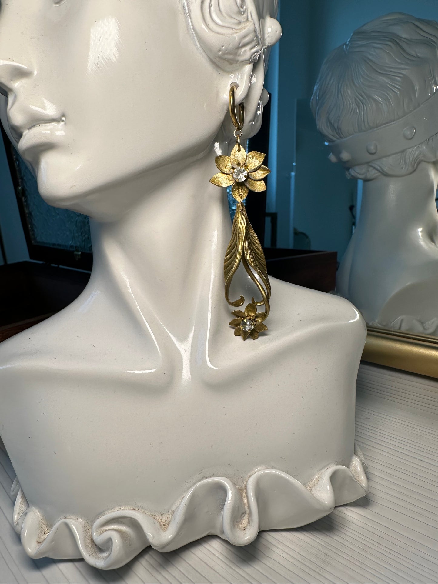 Close-up of long golden floral earrings with zirconia details, styled as timeless statement jewelry.
