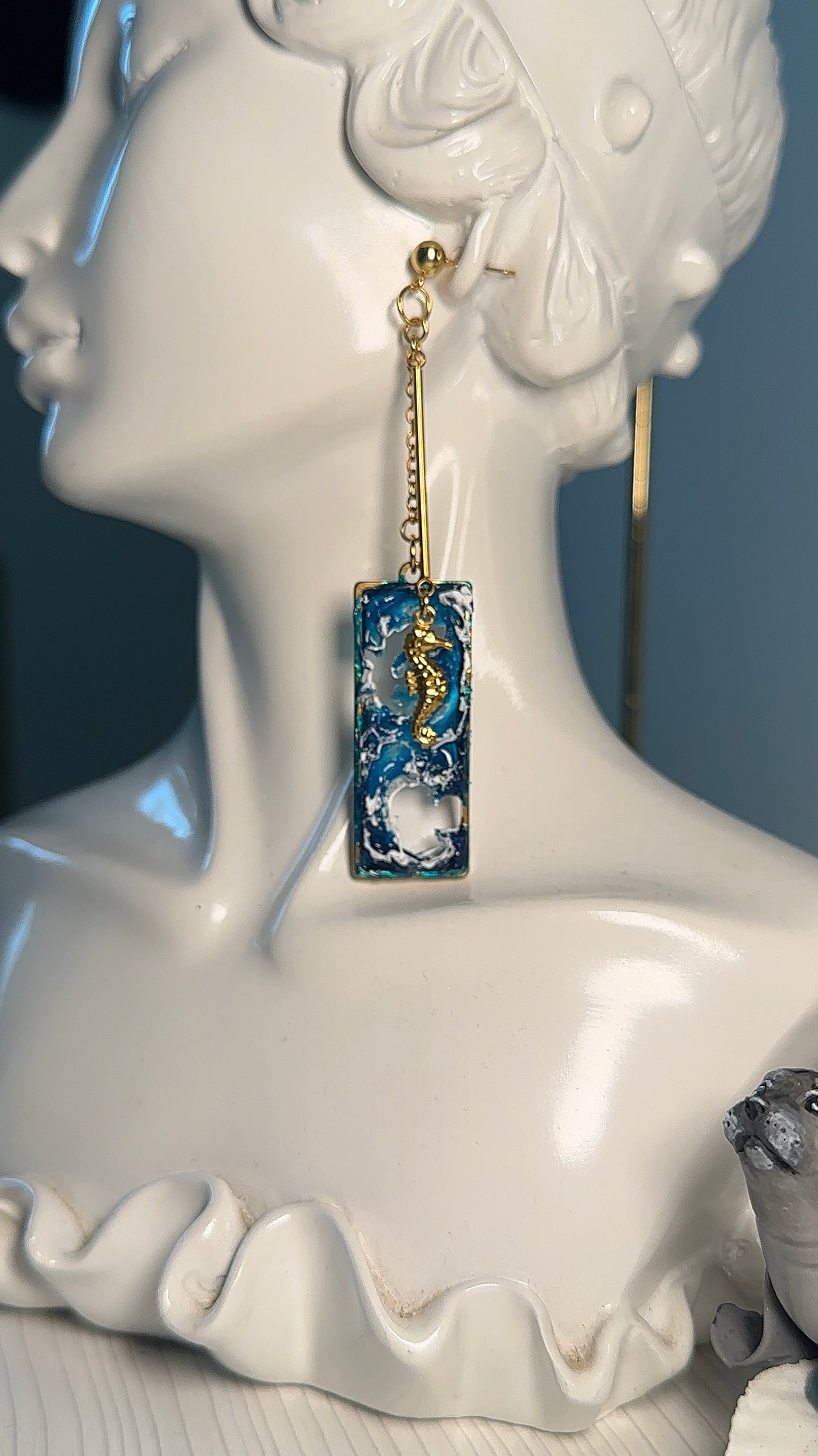 Artistic earrings with starfish and seahorse charms on a swirling blue sea background