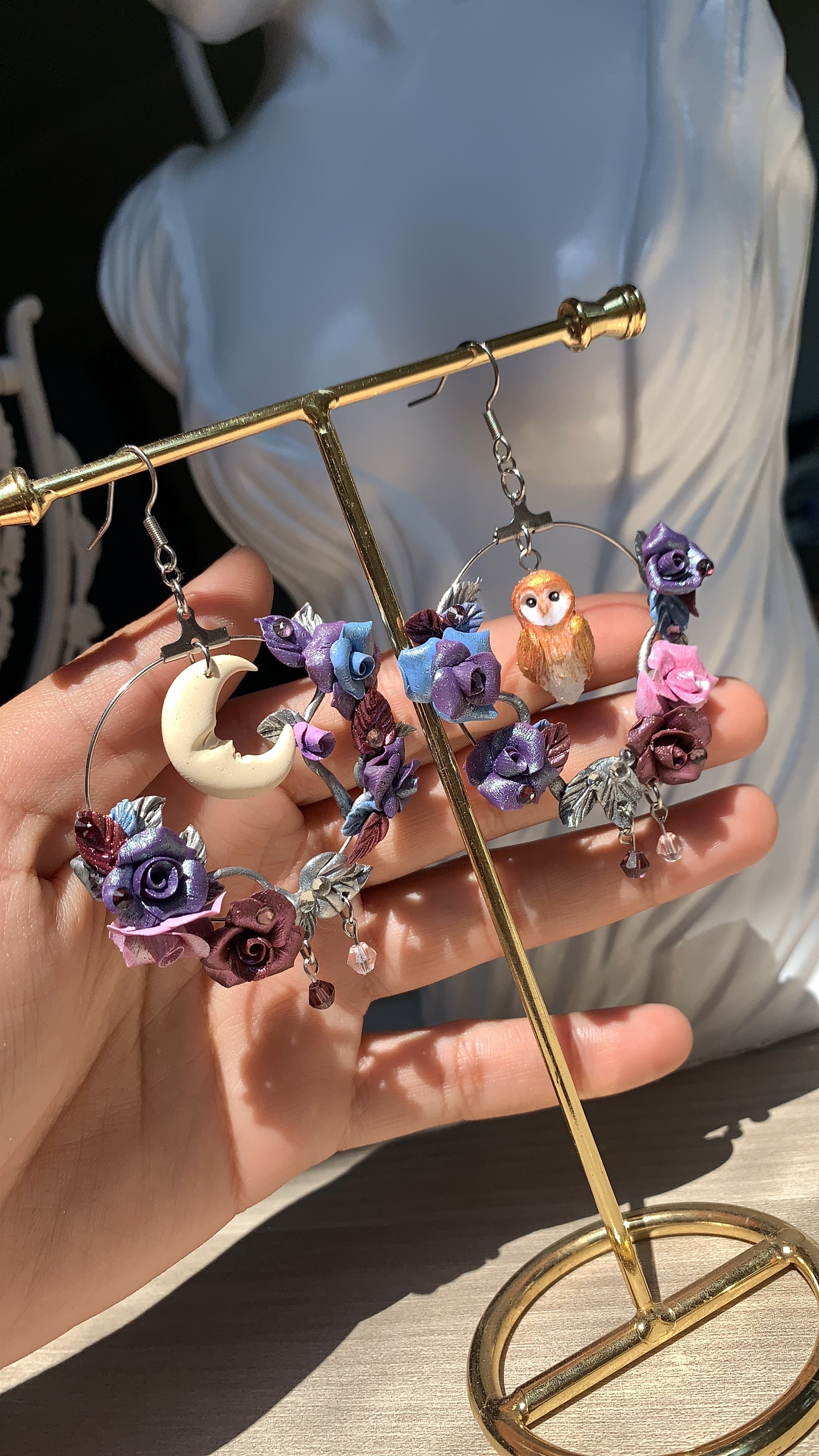 Artisan earrings with a forest owl nestled among polymer clay flowers and metallic leaves.