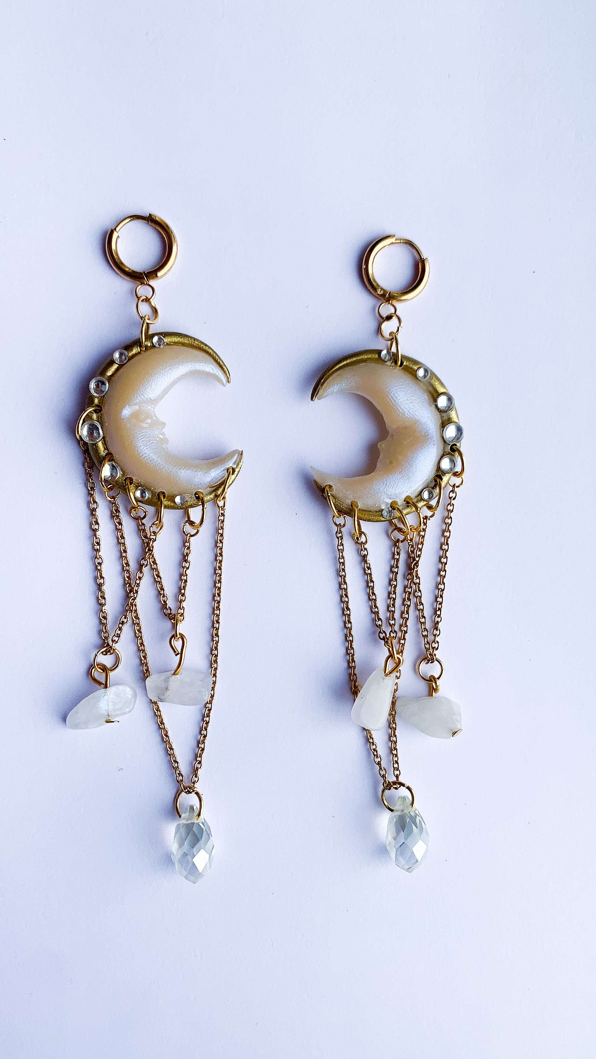 Dreamy moon-inspired earrings in pearly tones and gold chains, displayed on a sculptural mannequin.