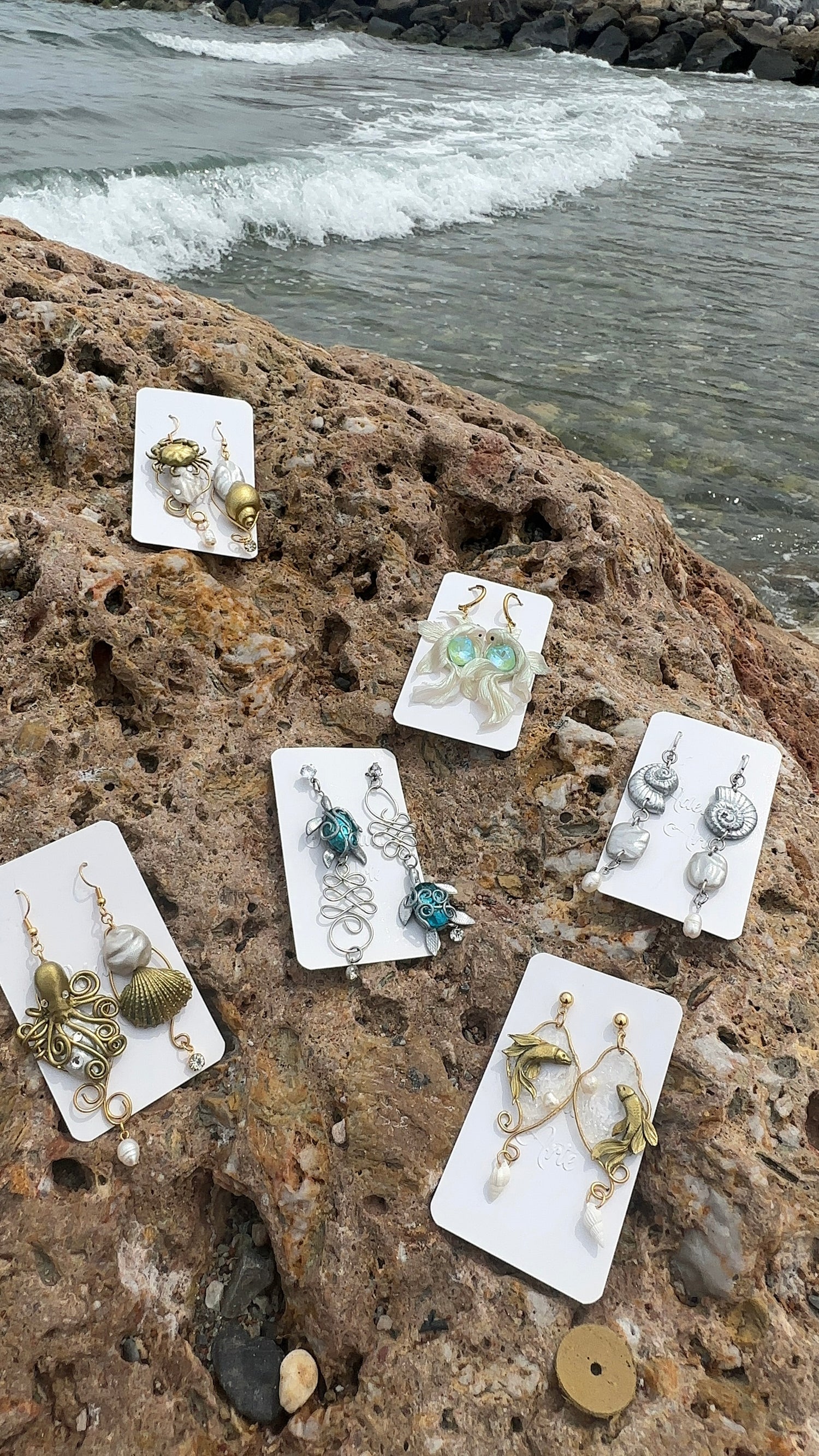 Asymmetrical handcrafted earrings inspired by the sea, featuring hand-sculpted waves, freshwater pearls, and marine charms in gold-toned stainless steel — part of the exclusive Unseen Waters collection.