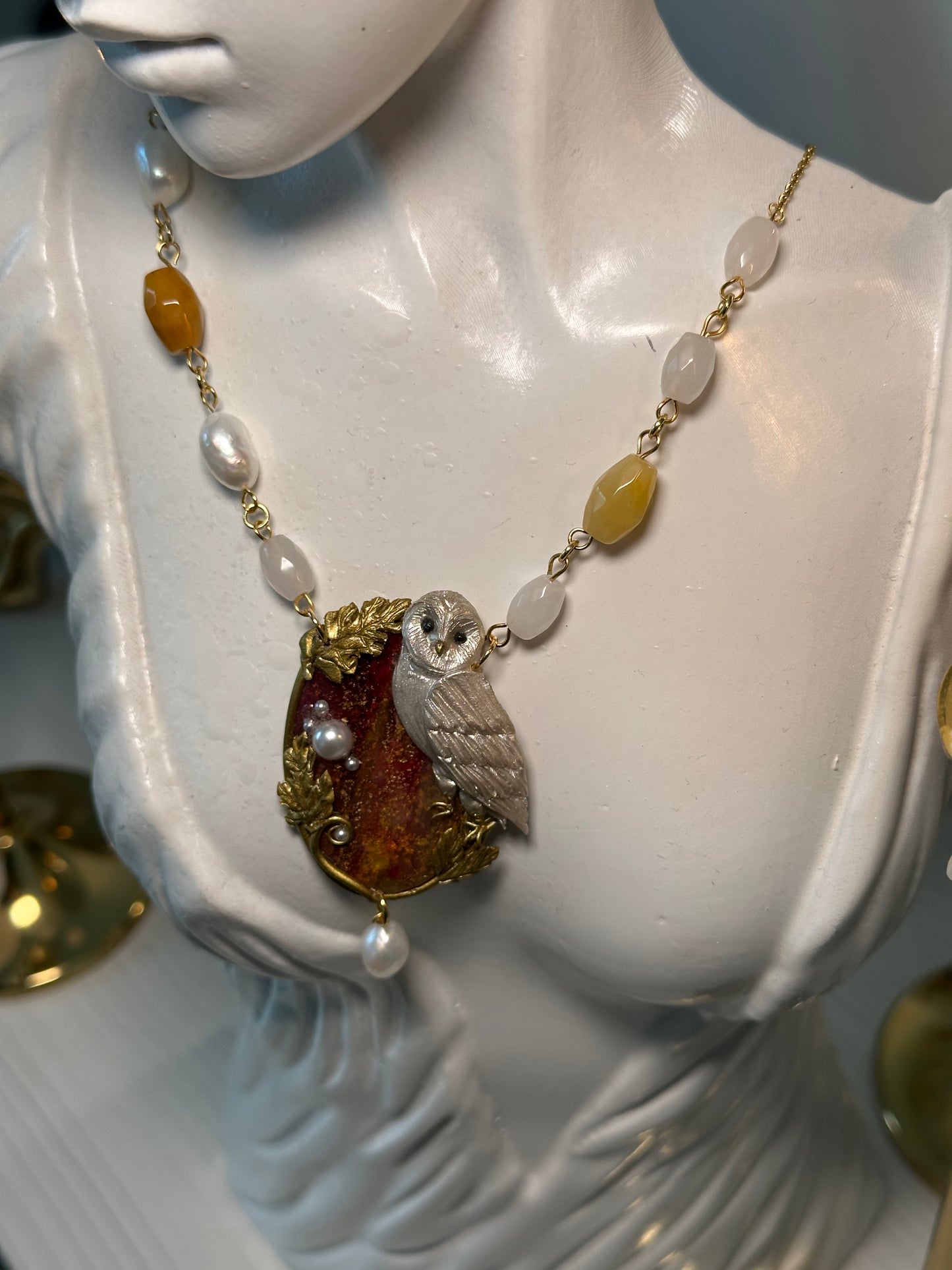 Elegant polymer clay owl pendant on a gemstone base, adorned with real pearls and gold leaves — artisanal jewelry for refined collectors.