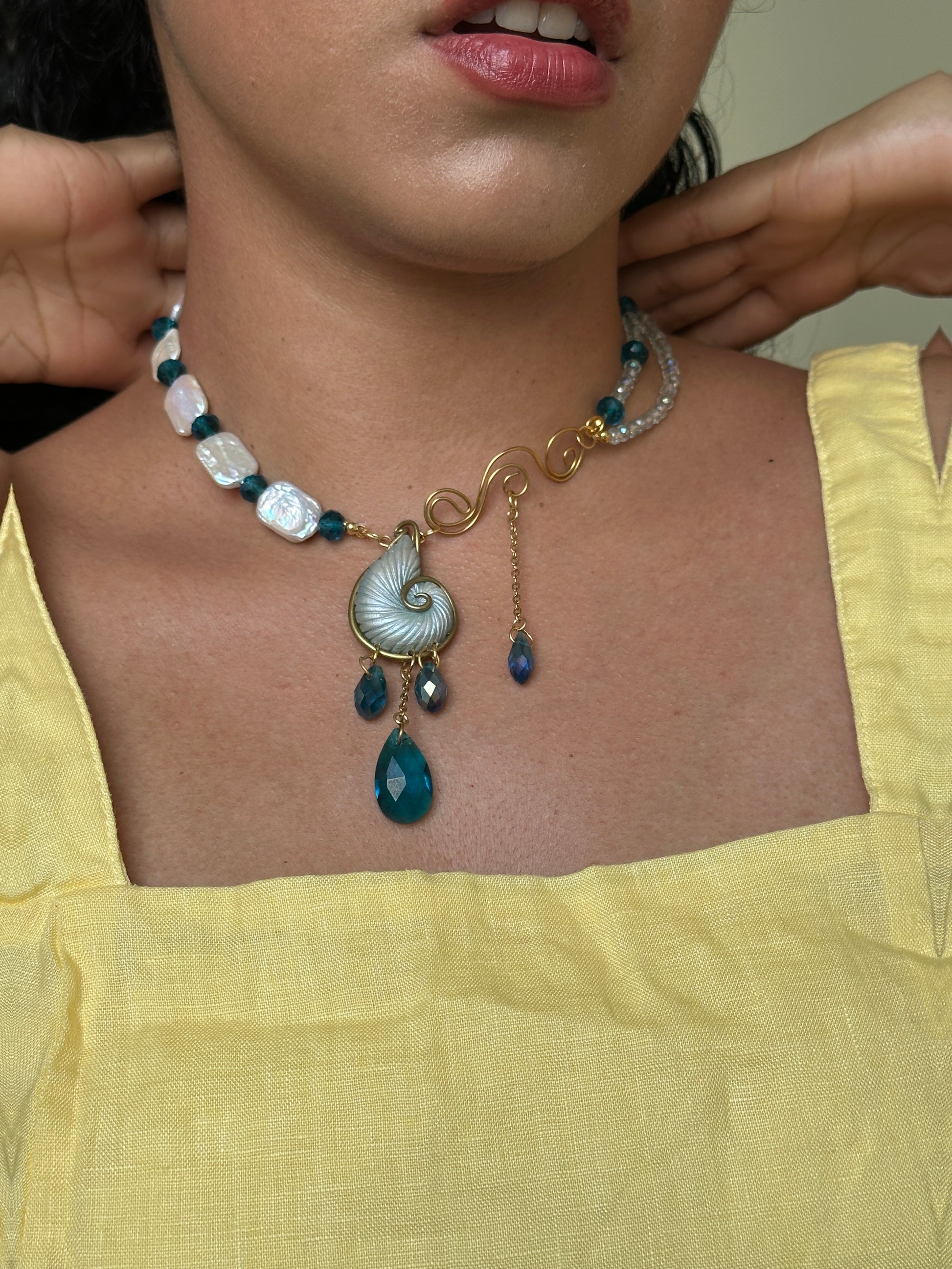     Handmade seashell statement necklace with gold scroll design, blue teardrop crystals and pearl beads, perfect for elegant summer outfits and unusual jewelry lovers.