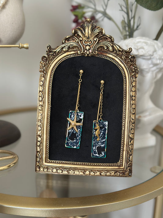 Close-up of asymmetrical ocean-inspired earrings with hand-sculpted waves and golden charms
