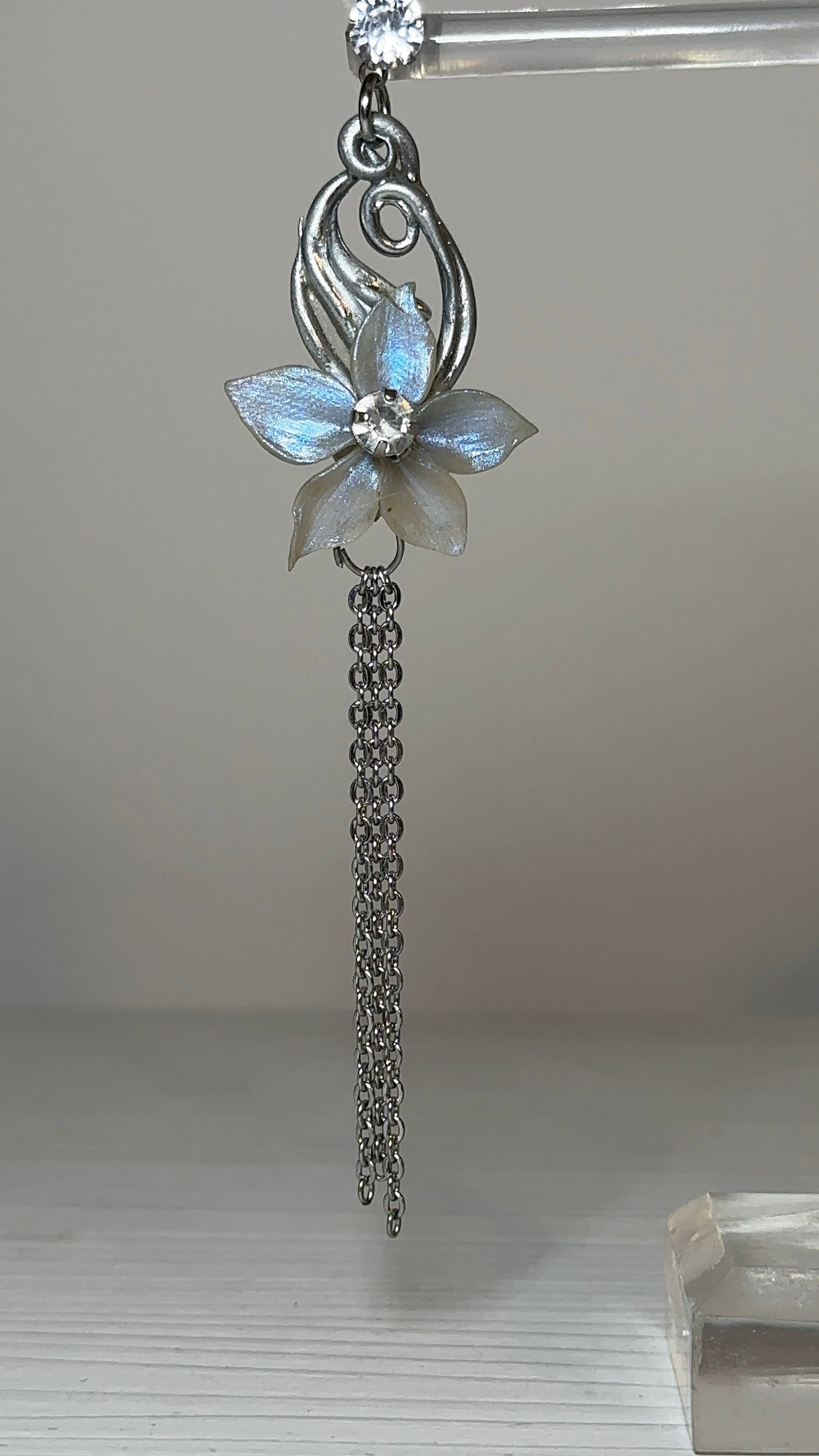 Delicate flower drop earrings with translucent petals and silver chains, styled on a porcelain bust to highlight their graceful movement and elegance.