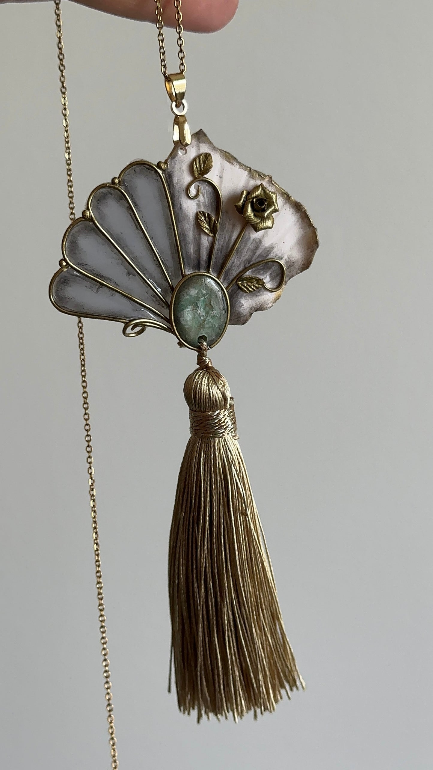     Sculptural fan pendant necklace with golden thread tassel and green stone-like detail, wearable art jewelry for women who love distinctive accessories.