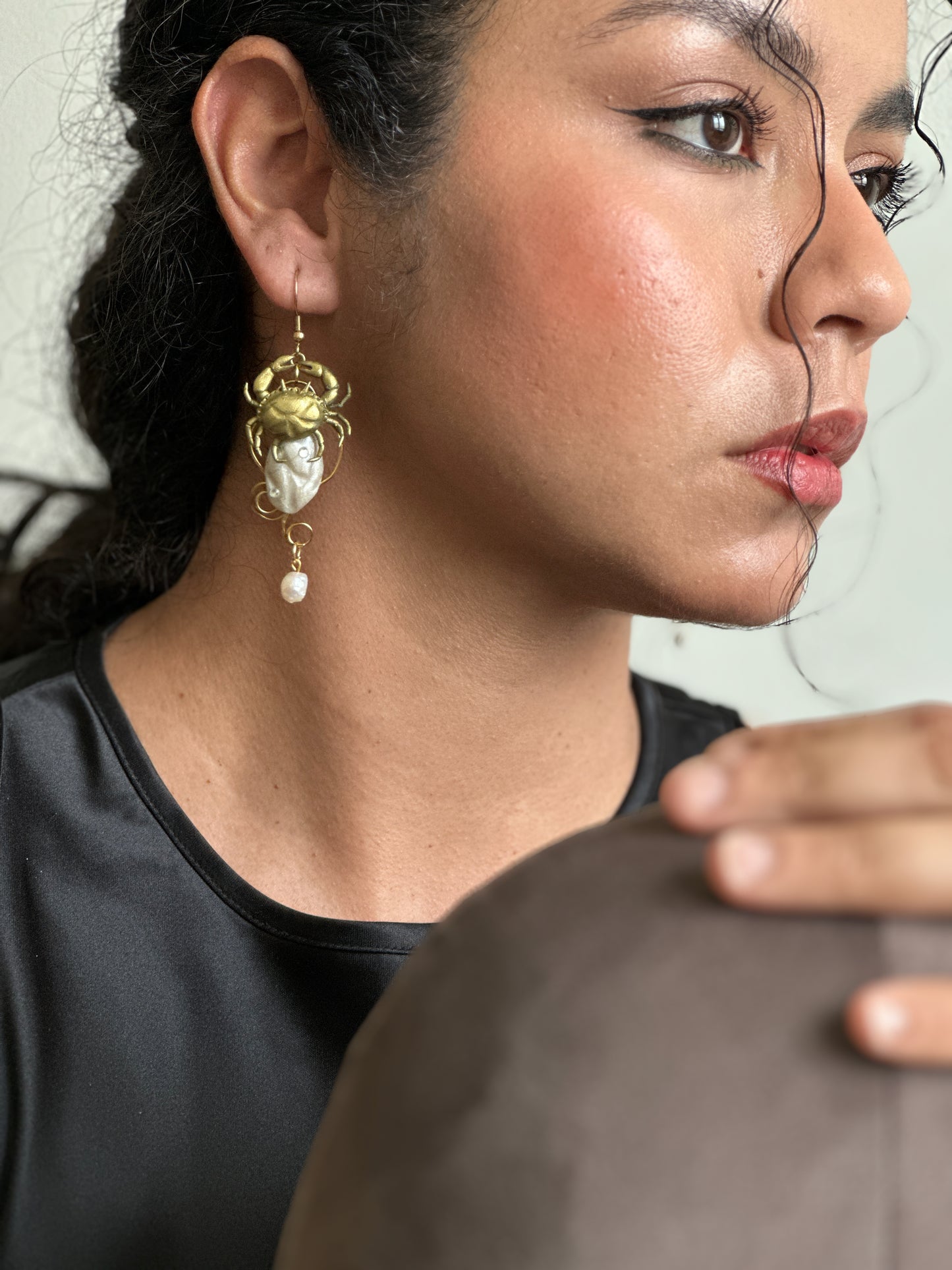     Handmade sculptural crab and shell earrings in gold and pearl tones, worn with a simple black dress to make a minimal outfit feel intentional and unforgettable.