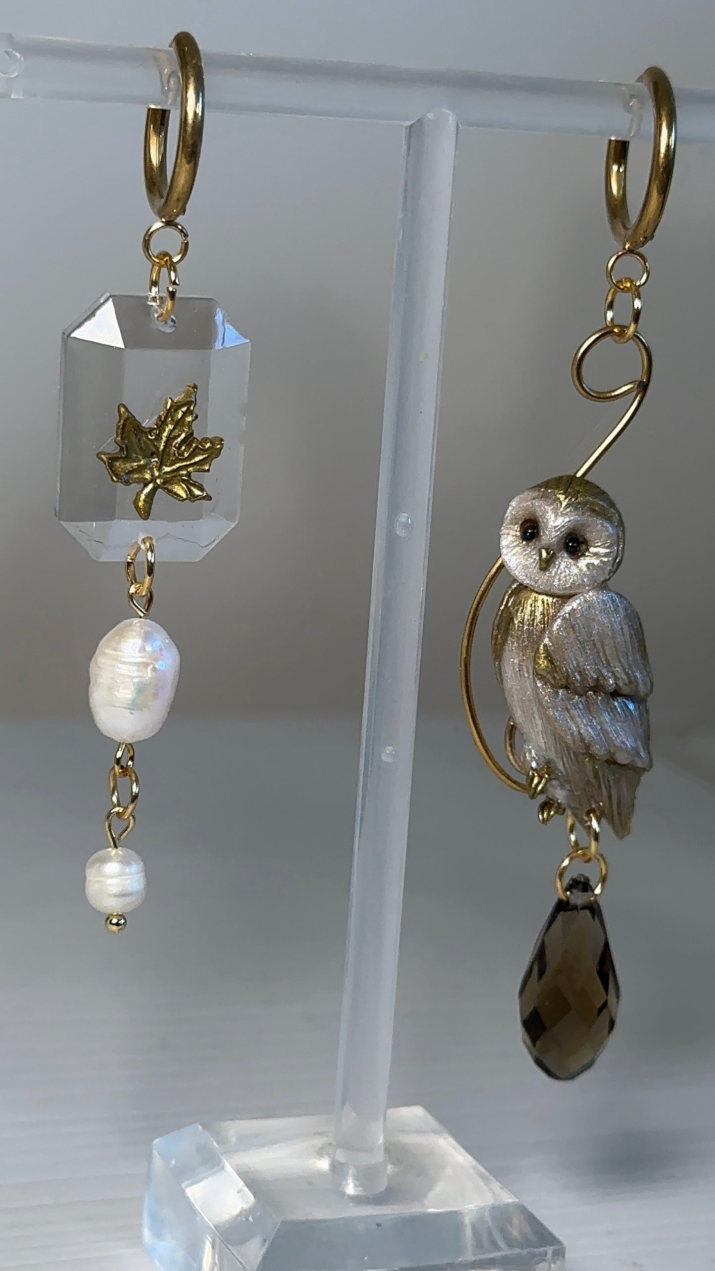 Fine handcrafted earrings combining a sculpted owl, maple leaf, and luminous pearls — an artistic asymmetrical composition.