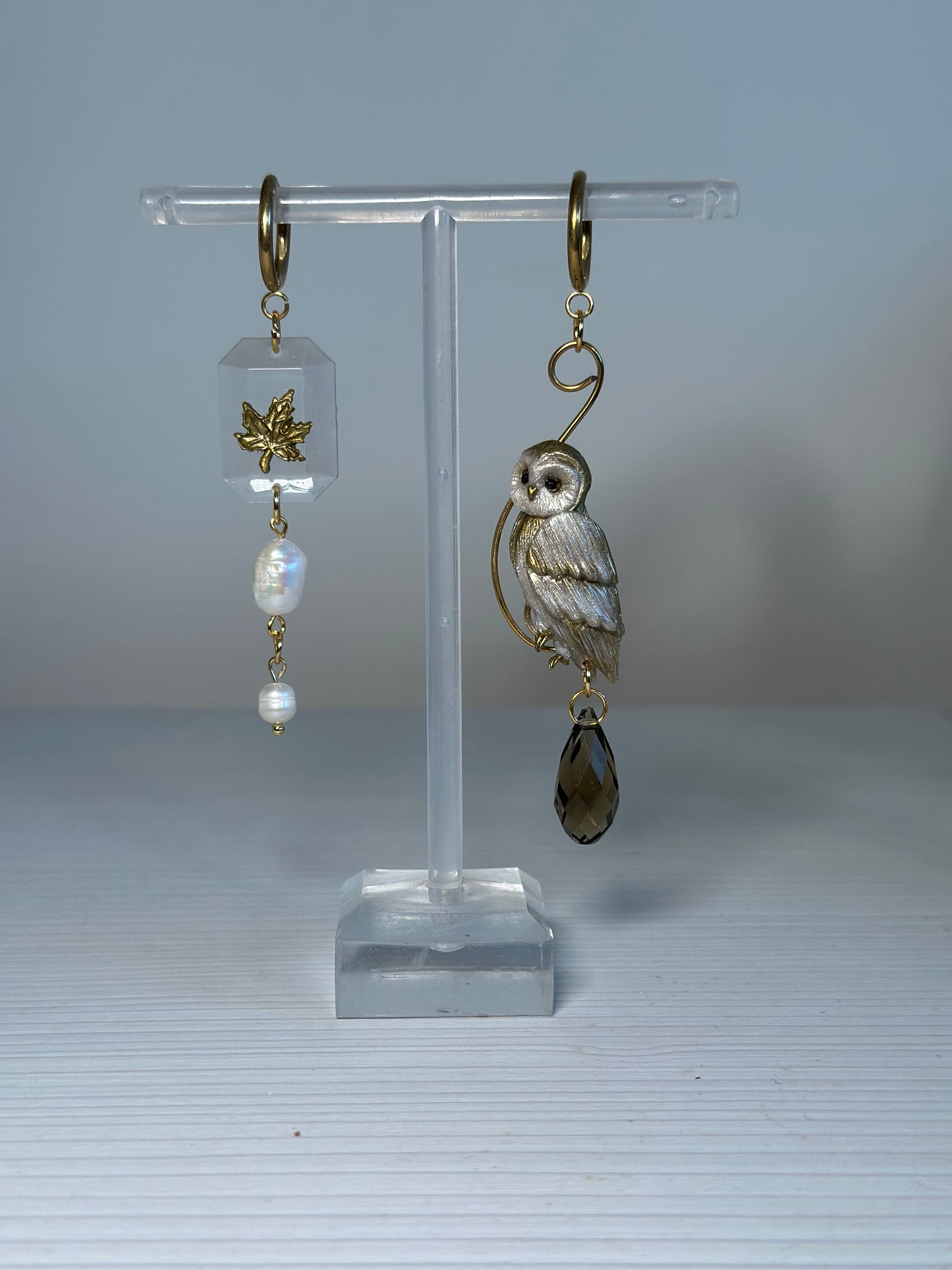 Asymmetrical earrings featuring a hand-sculpted golden owl and maple leaf charm with natural pearls and crystals, stainless steel findings