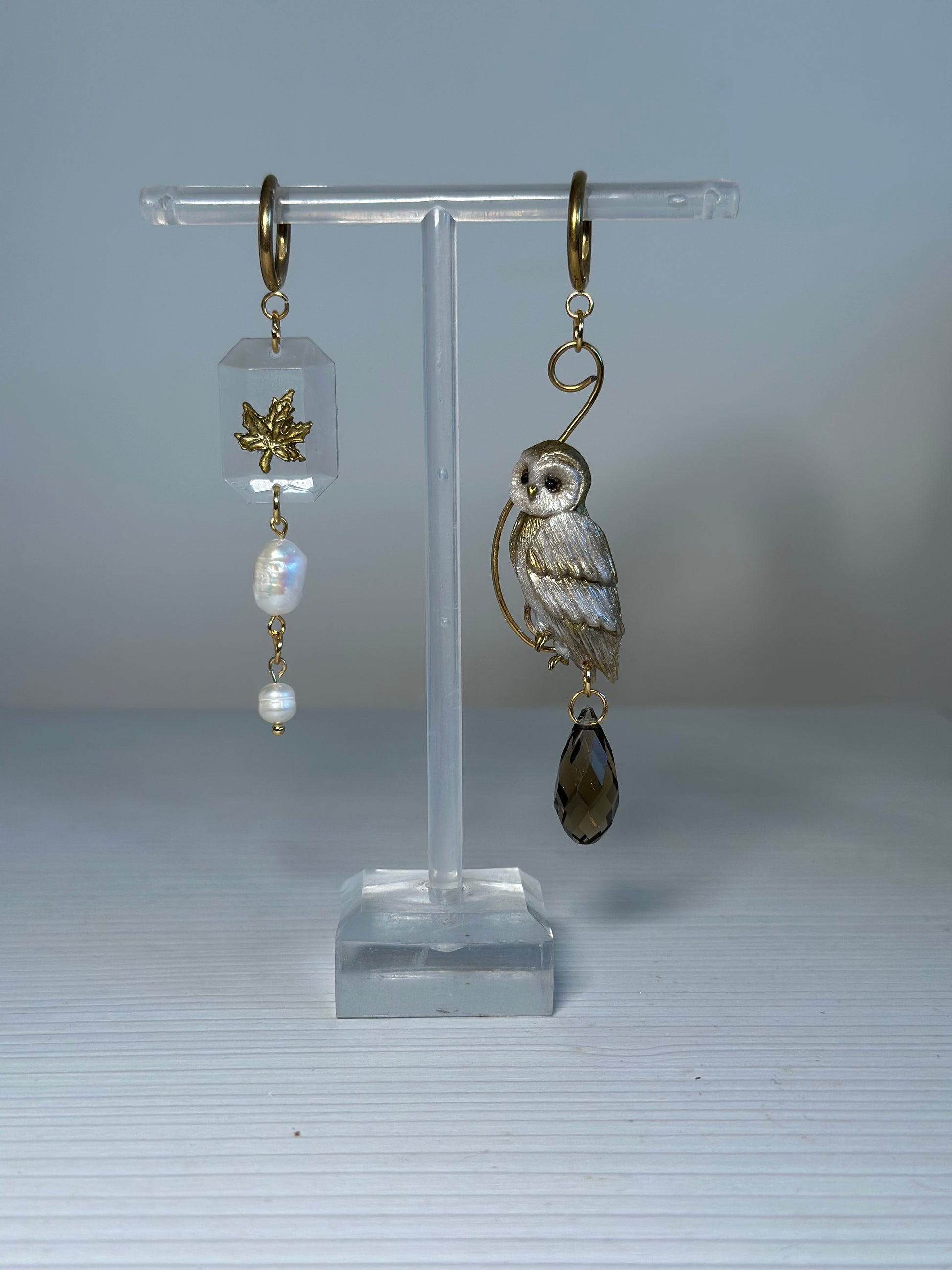 Asymmetrical earrings featuring a hand-sculpted golden owl and maple leaf charm with natural pearls and crystals, stainless steel findings