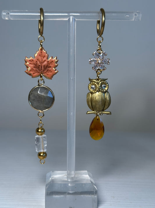 Asymmetrical handcrafted earrings featuring a golden owl and a maple leaf charm, made in polymer clay with stainless steel findings, labradorite, and crystal beads.