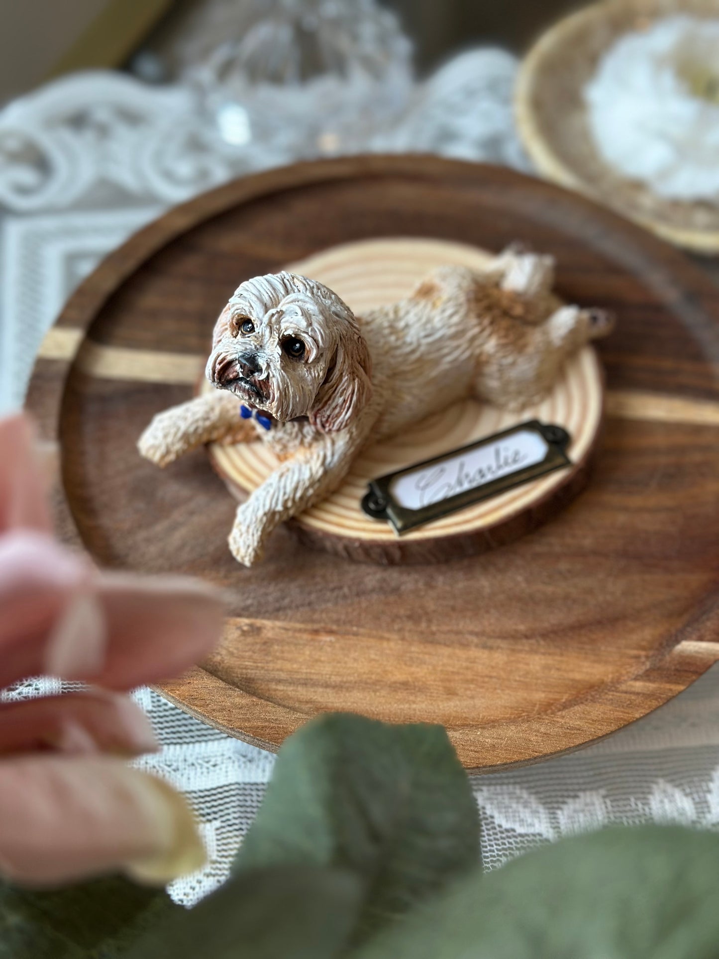 Detailed custom pet sculpture of a fluffy dog lying peacefully on a wood pedestal with a nameplate. Soft floral background and refined textures, created for pet lovers who value emotional keepsakes and quiet luxury.
