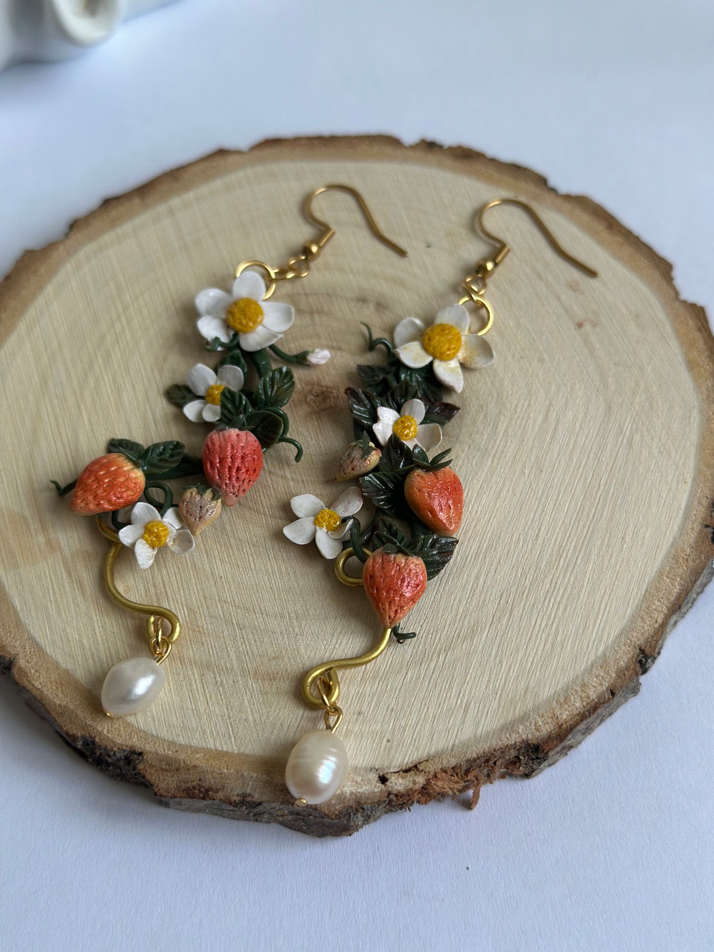 Orecchino artigianale in pasta polimerica con fragole, fiori bianchi, filo dorato e perla. Gioiello botanico romantico.
Handmade polymer clay earring with strawberries, white flowers, gold wire, and pearl. Botanical romantic jewelry.
