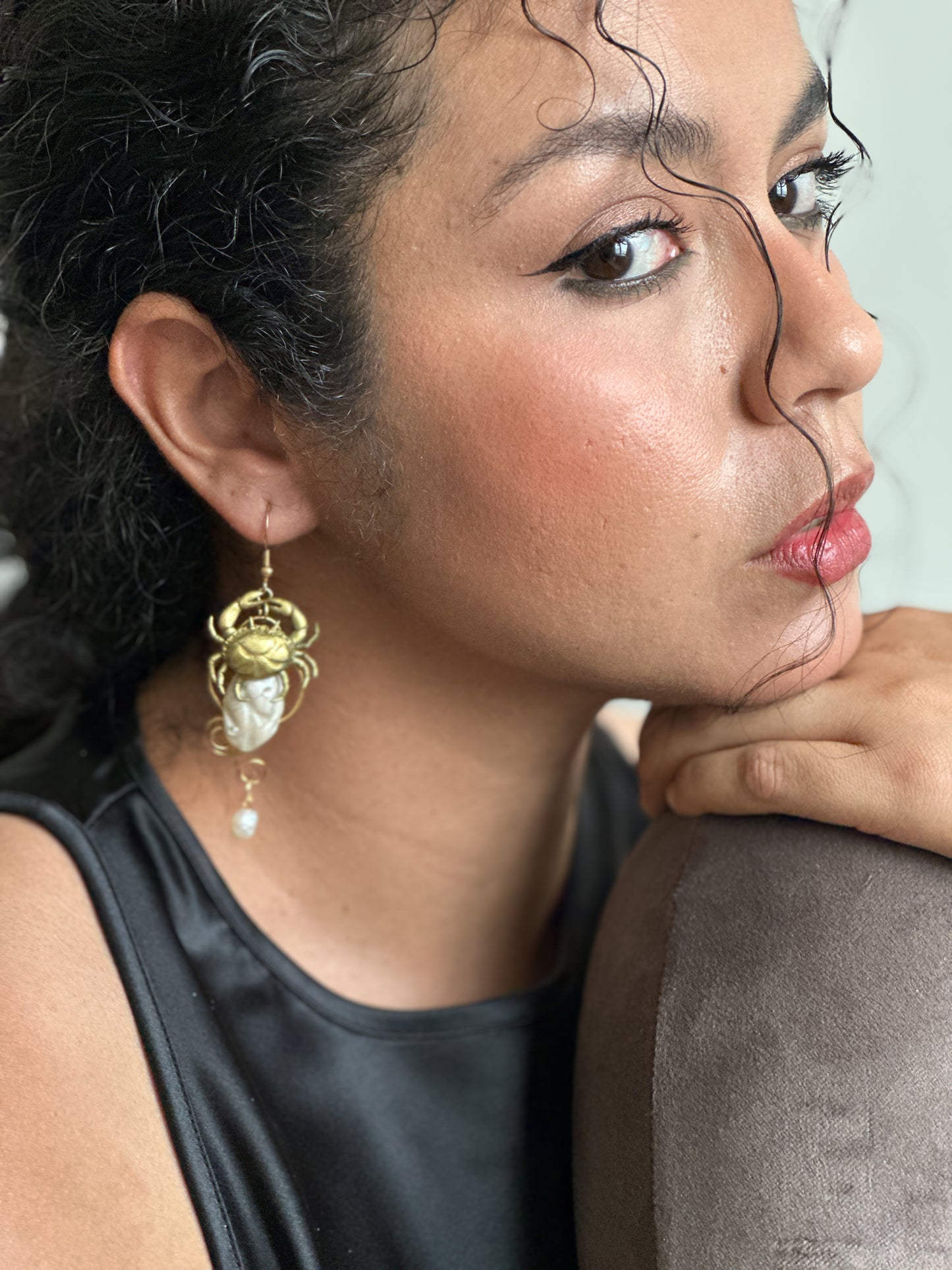     Close-up of statement ocean-inspired earrings with a golden crab, shell details and dangling pearls, adding personality to a plain black summer look.
