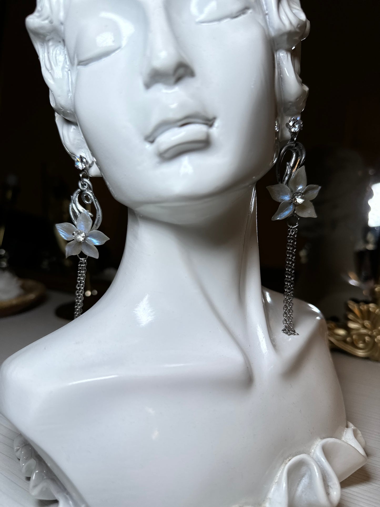 Elegant floral drop earrings with translucent petals, silver accents, and delicate chain details, displayed on a classical bust for a refined, timeless look.