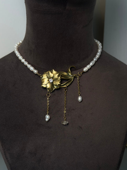 Artistic gold flower necklace with pearl chain and dangling details, sculptural botanical jewelry piece for elegant outfits