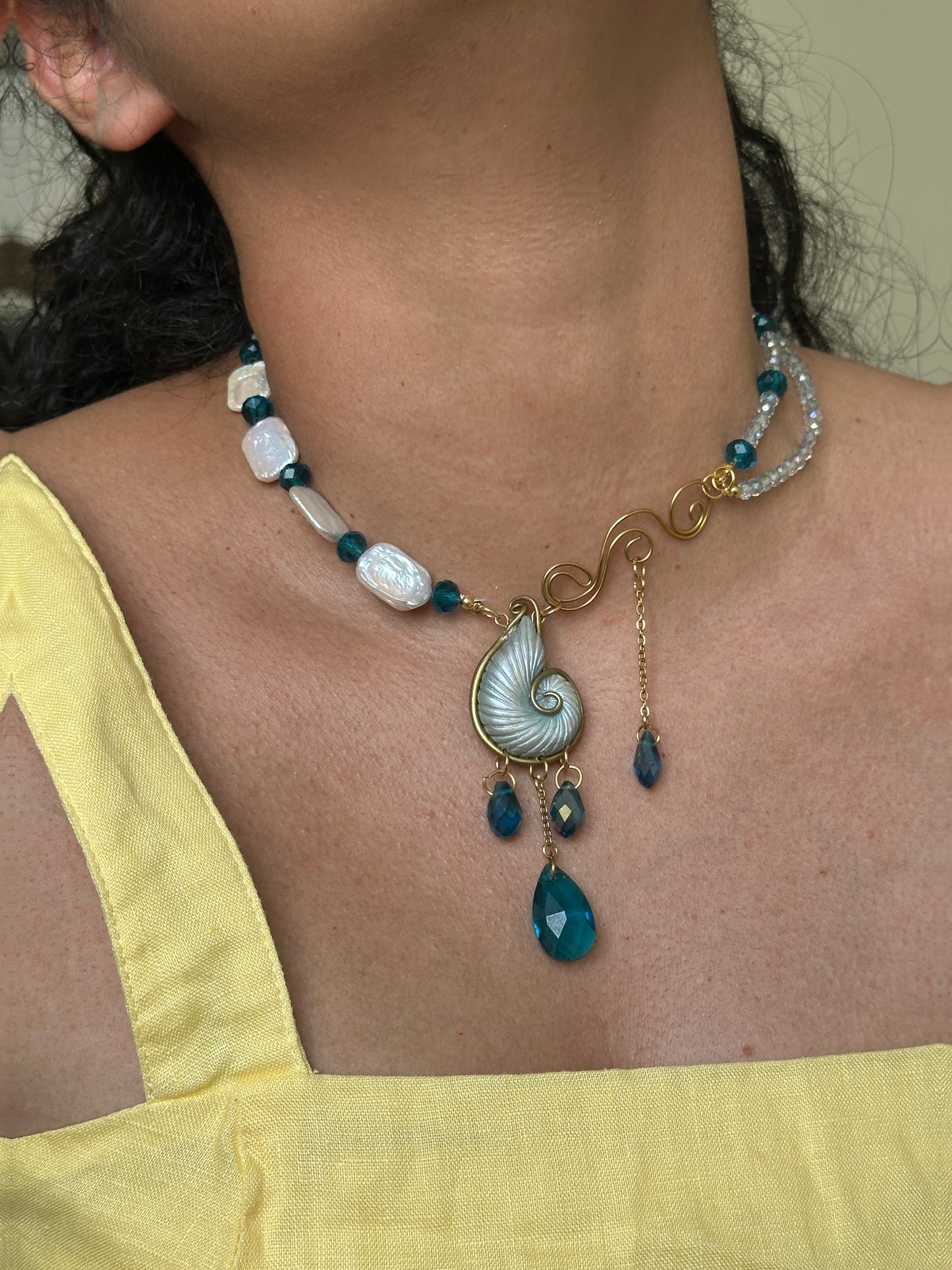     Ocean inspired sculptural necklace with spiral shell pendant, blue beads, pearl accents and gold details, a unique handmade statement piece for women.