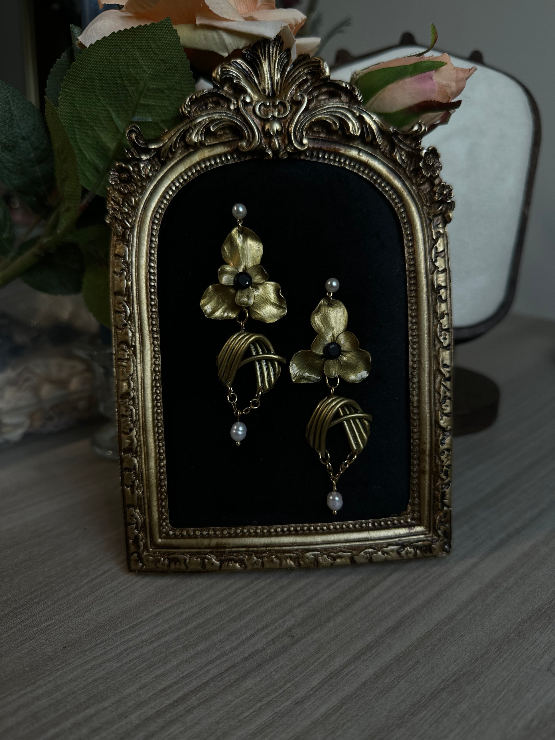 Orecchini dorati unici con forme floreali scolpite a mano e gocce di perla, presentati come parte di una collezione elegante.