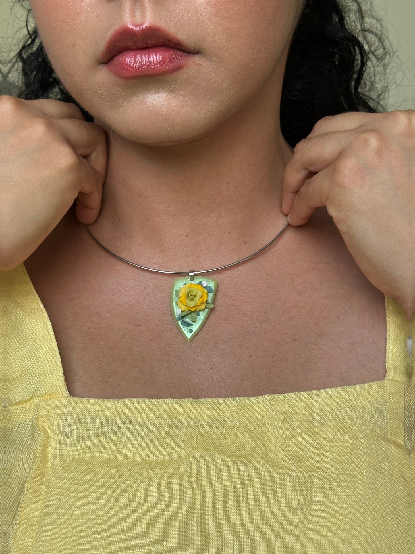     Handmade yellow rose sculptural pendant necklace on soft green base, styled with a yellow linen dress for a romantic botanical summer look.