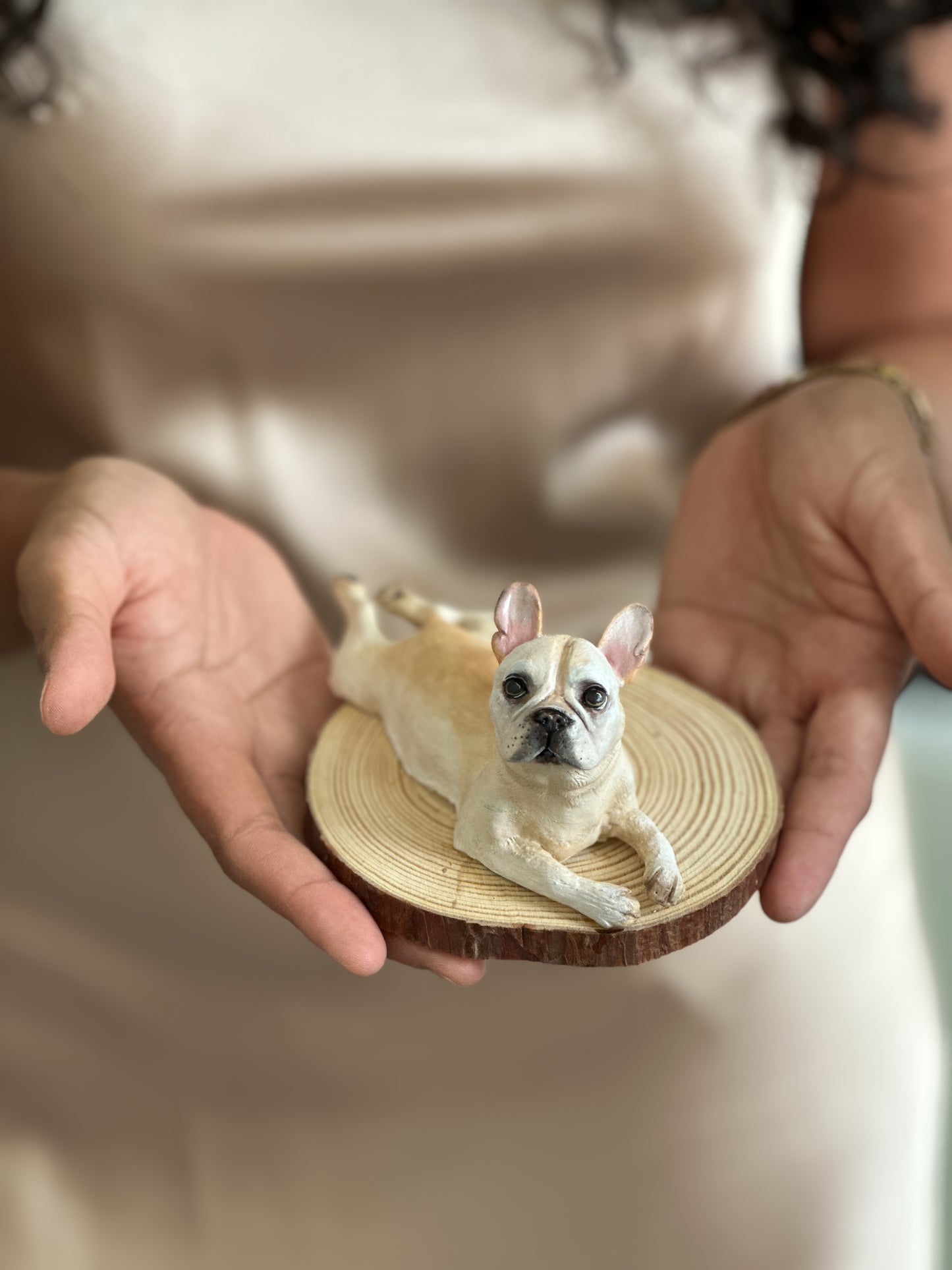 Close-up of a lifelike French Bulldog sculpture handmade from clay, featuring expressive eyes, soft cream coloring, and realistic details on a rustic wooden base.